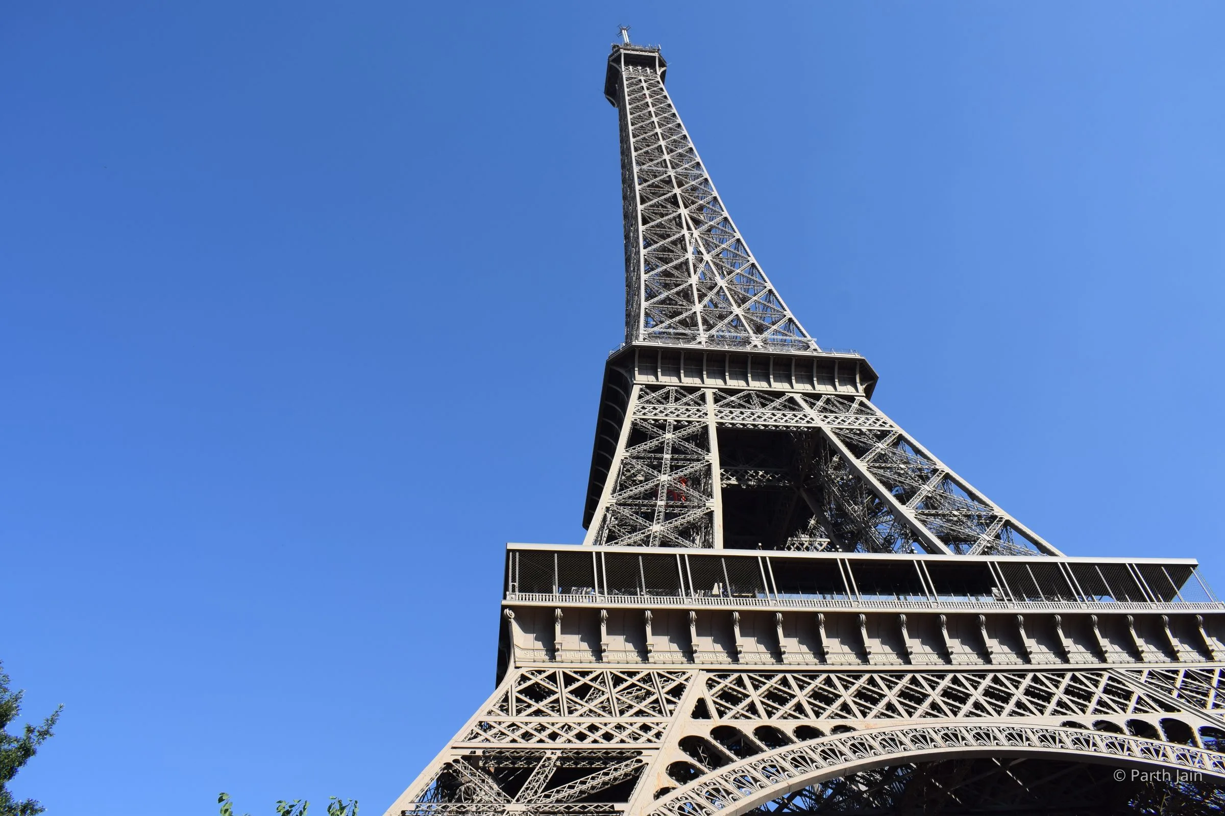 The Eiffel Tower from directly beneath, the lattice rising into a clear blue sky.