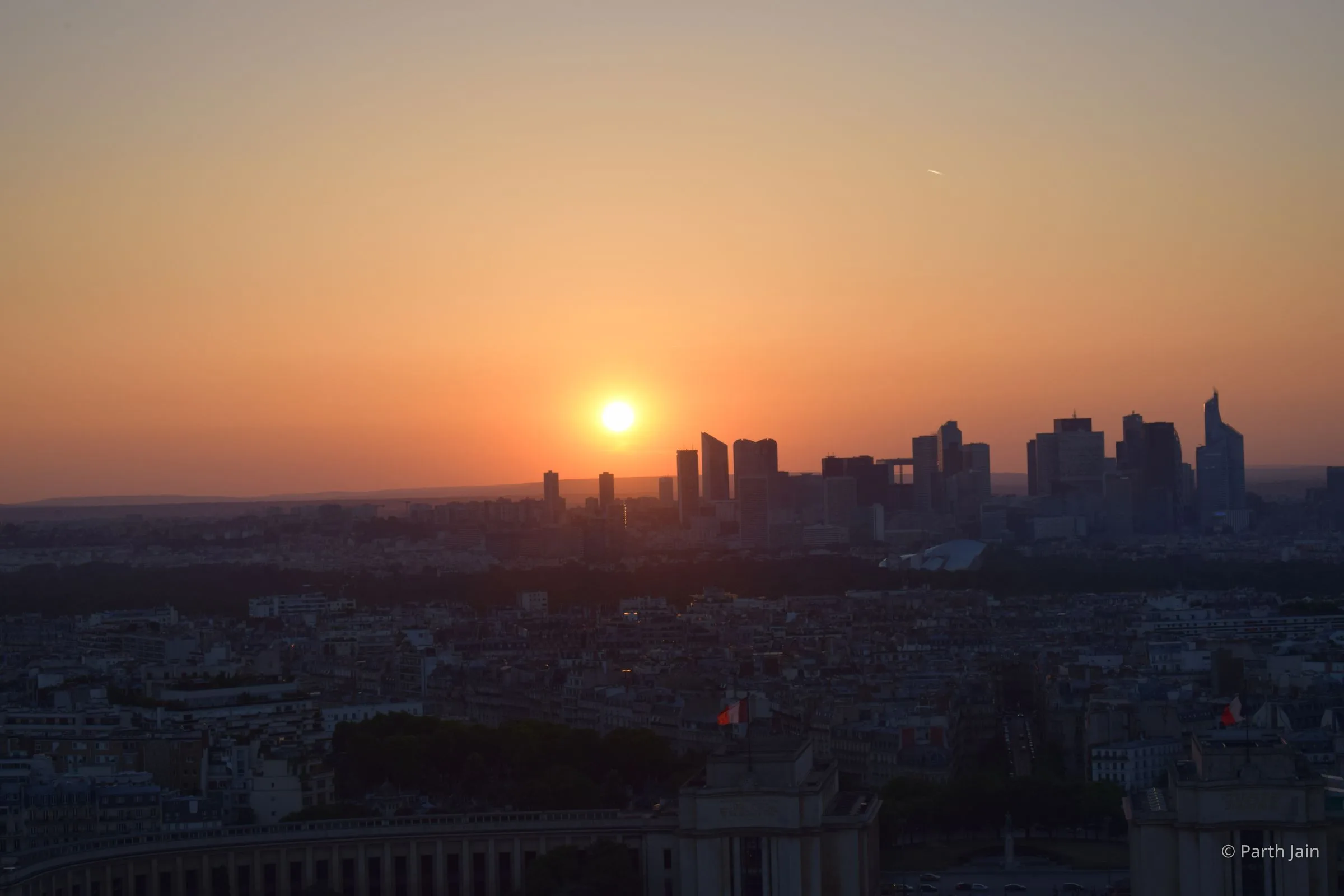 Sunset over La Défense from the Eiffel Tower, sun sitting just above the silhouetted skyscrapers.