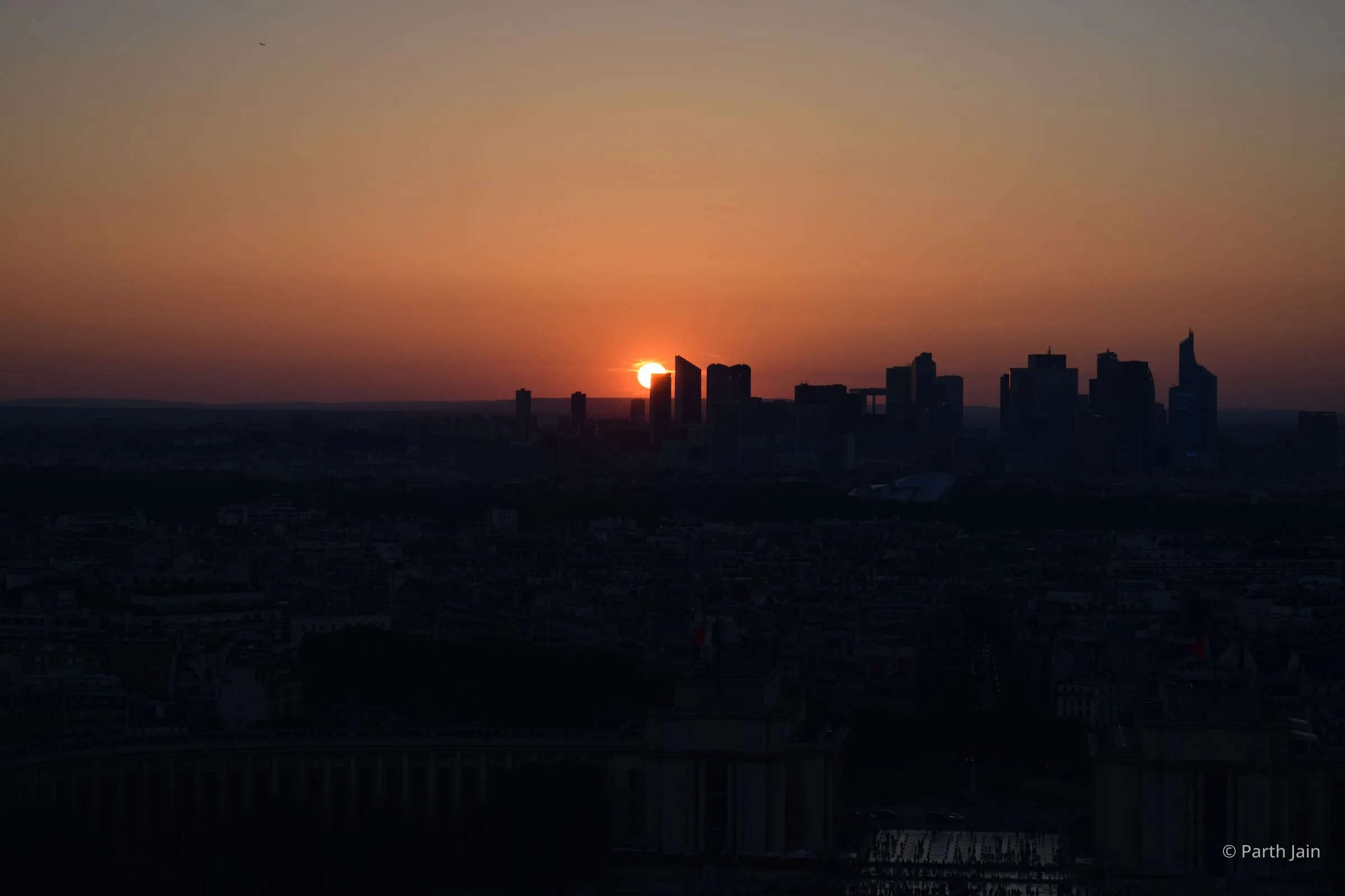 Sunset over La Défense a few minutes later, sun half-disappeared behind a tower, sky deep red-orange.