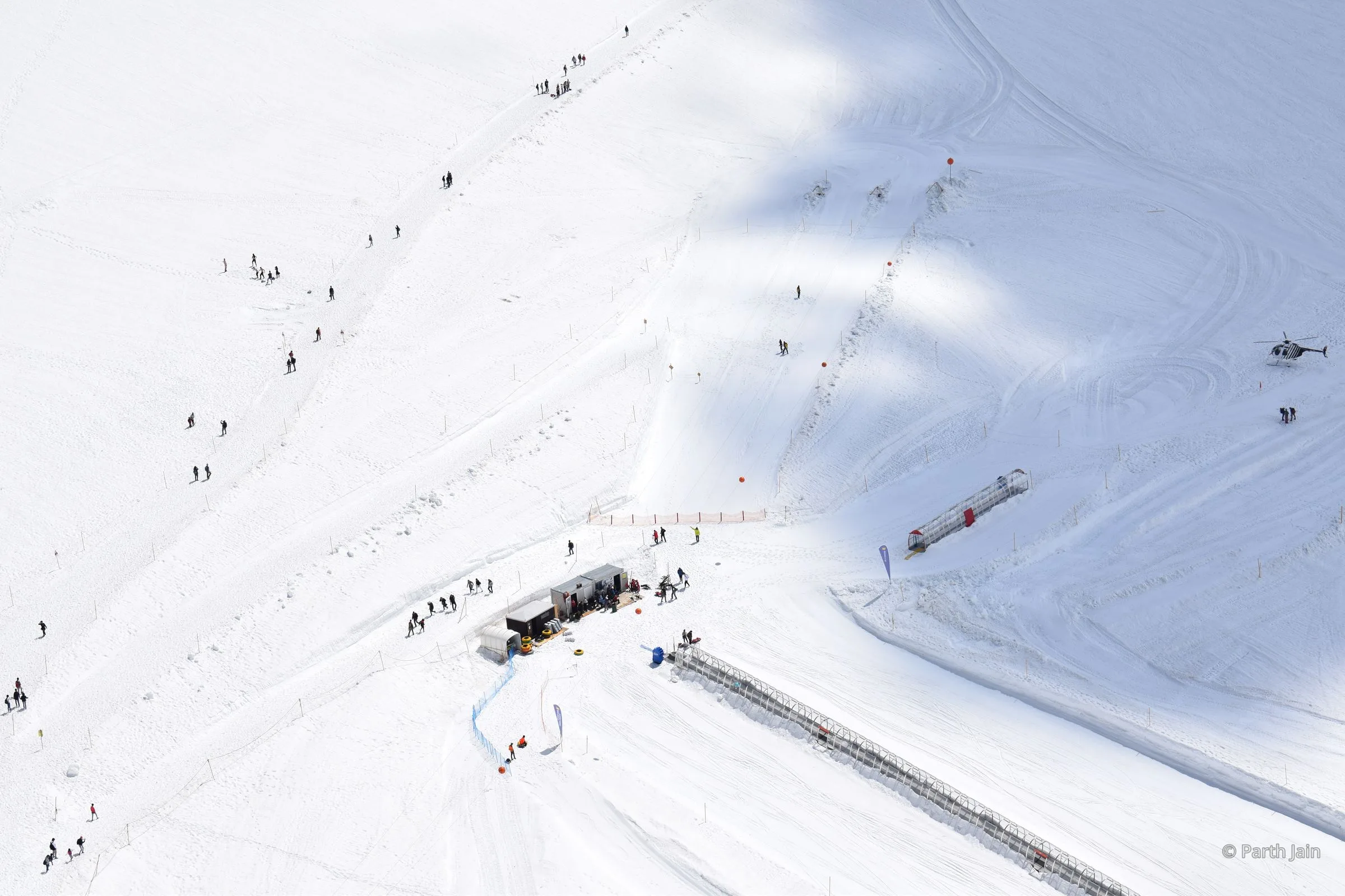 A small helicopter crossing a vast snowfield, seen from above.