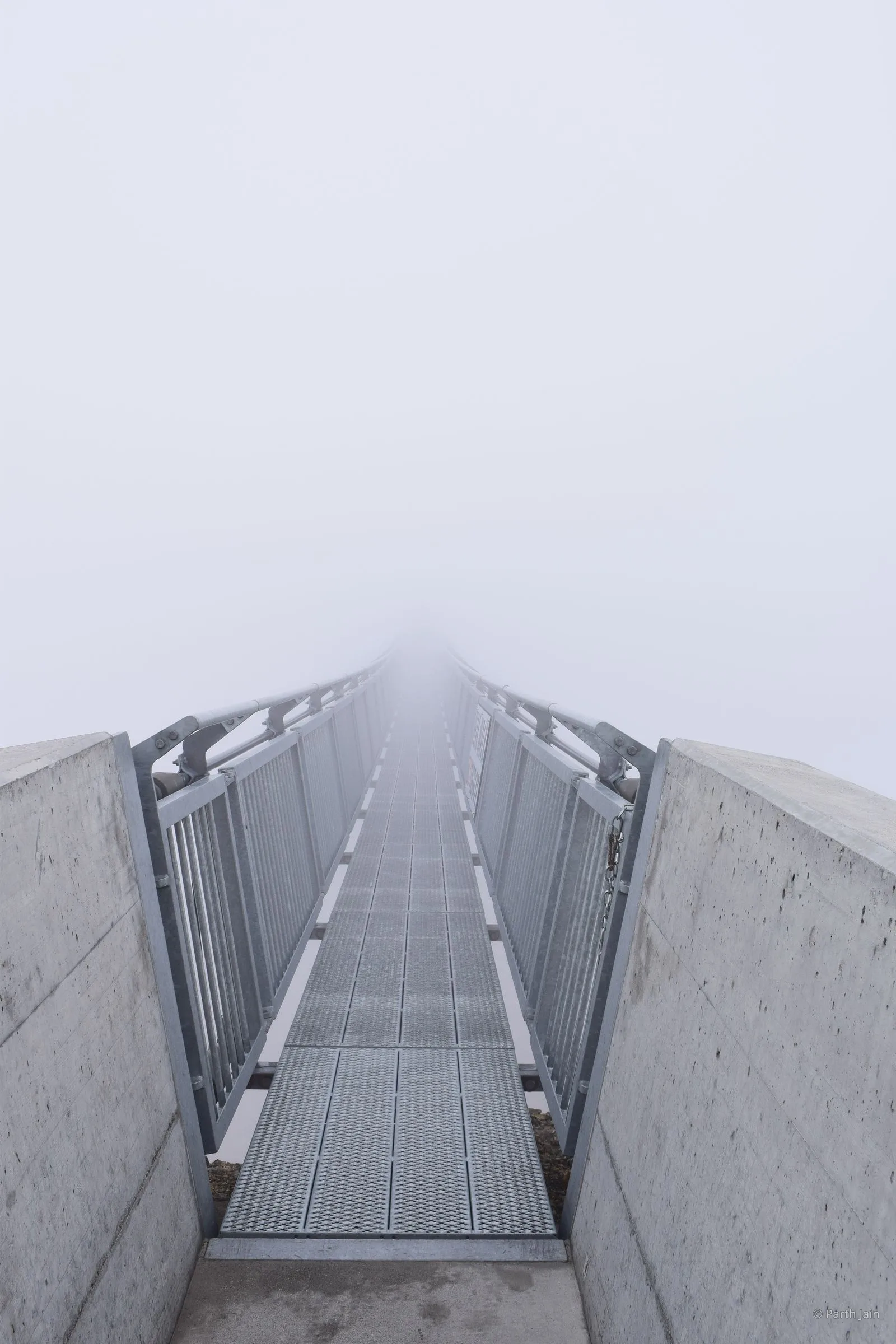 The Peak Walk suspension bridge at Glacier 3000, both summits faintly visible through fog.