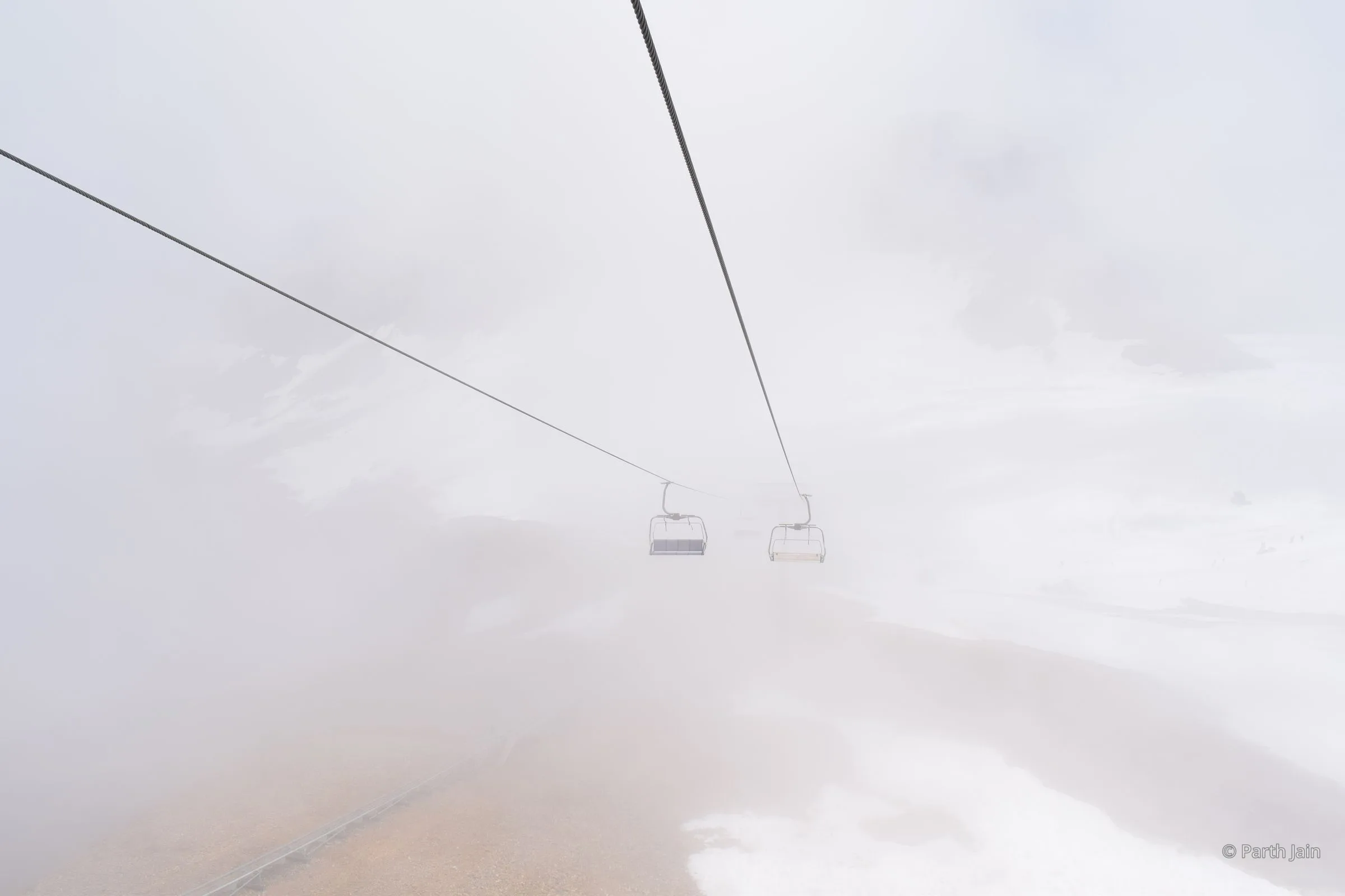 A row of empty chairlifts disappearing into fog.